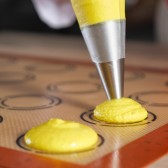 Pochage de macarons jaunes sur tapis silicone.