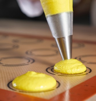 Pochage de macarons jaunes sur tapis silicone.